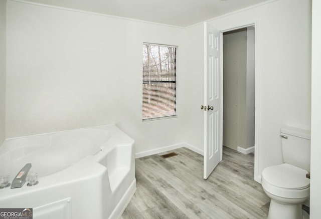 bathroom featuring wood finished floors, a garden tub, toilet, and baseboards