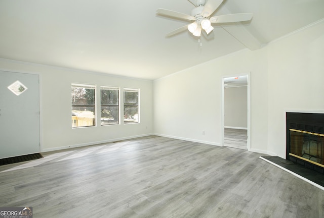 unfurnished living room with ornamental molding, a glass covered fireplace, baseboards, and light wood finished floors