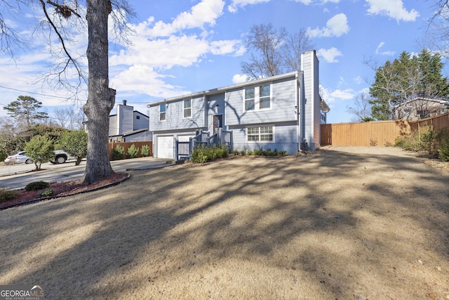 split foyer home featuring a garage, concrete driveway, fence, and a chimney