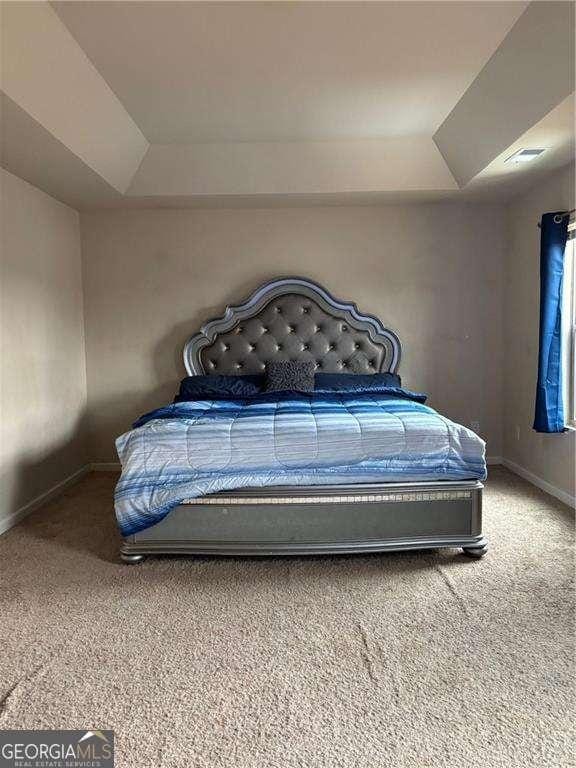 bedroom featuring a tray ceiling, carpet flooring, visible vents, and baseboards