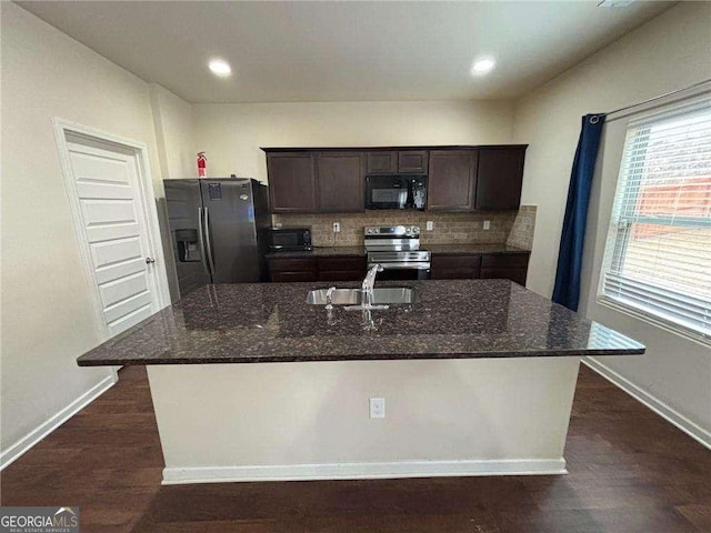 kitchen featuring dark stone counters, stainless steel appliances, a sink, and a center island with sink