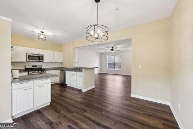 kitchen featuring stone countertops, white cabinets, open floor plan, hanging light fixtures, and appliances with stainless steel finishes