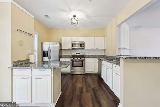 kitchen featuring stainless steel appliances, a peninsula, a sink, white cabinets, and dark stone counters