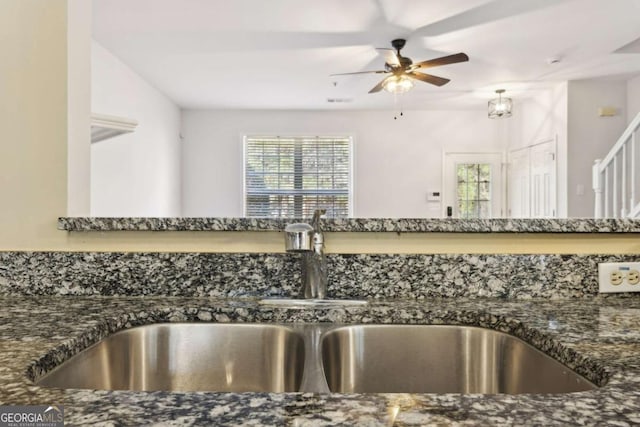 kitchen with a ceiling fan, dark stone counters, and a sink