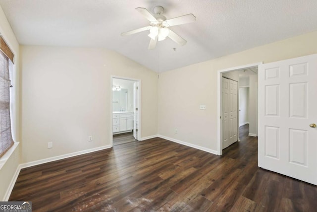 unfurnished bedroom with lofted ceiling, dark wood finished floors, baseboards, and ensuite bathroom