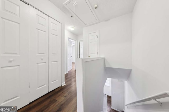 hallway featuring attic access, dark wood-style flooring, and an upstairs landing