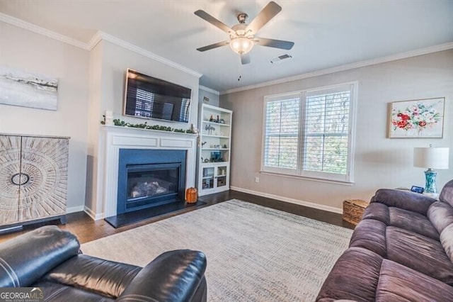 living room featuring visible vents, ornamental molding, a glass covered fireplace, wood finished floors, and baseboards