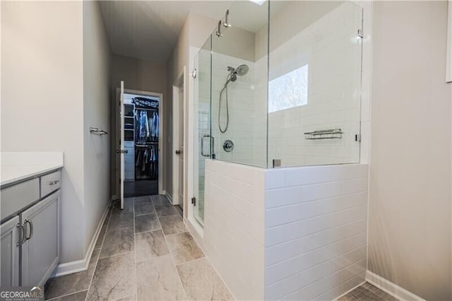 full bath featuring a spacious closet, a stall shower, vanity, and baseboards