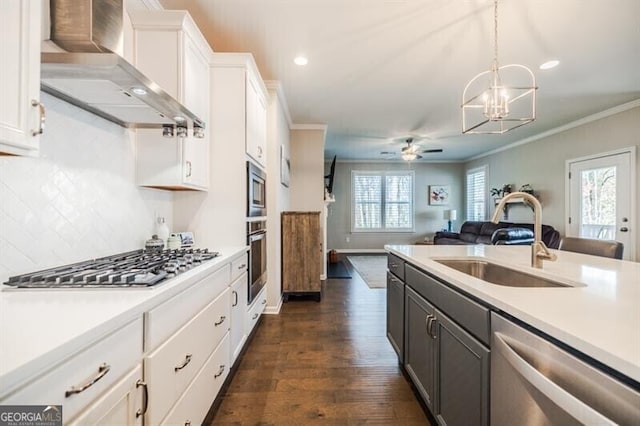 kitchen featuring wall chimney exhaust hood, ornamental molding, stainless steel appliances, light countertops, and a sink