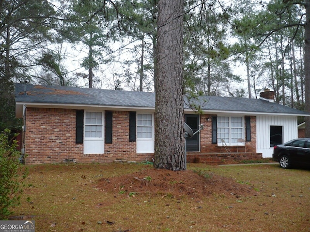 ranch-style house featuring a front yard, a chimney, and brick siding