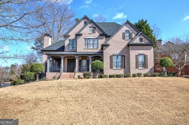 view of front of property with a front yard, covered porch, brick siding, and a chimney