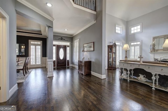 foyer entrance with decorative columns, a high ceiling, dark wood-type flooring, ornamental molding, and baseboards