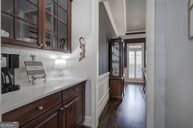 kitchen with dark wood-style flooring, light countertops, decorative backsplash, ornamental molding, and glass insert cabinets