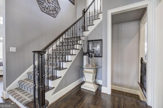 stairs featuring a towering ceiling, baseboards, and wood finished floors