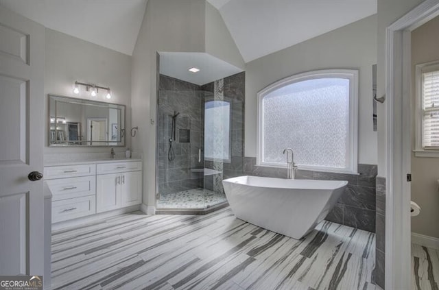 bathroom with a stall shower, vaulted ceiling, a freestanding bath, vanity, and tile walls