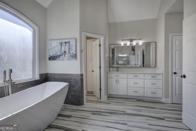 full bathroom with a freestanding bath, vaulted ceiling, vanity, and tile walls