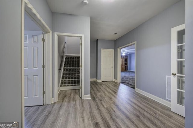 hallway with stairs, visible vents, baseboards, and wood finished floors