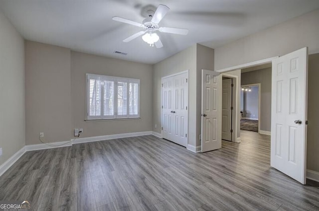 unfurnished bedroom featuring ceiling fan, wood finished floors, visible vents, baseboards, and a closet