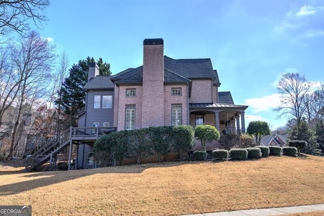 view of side of property featuring brick siding, a lawn, a chimney, and stairs