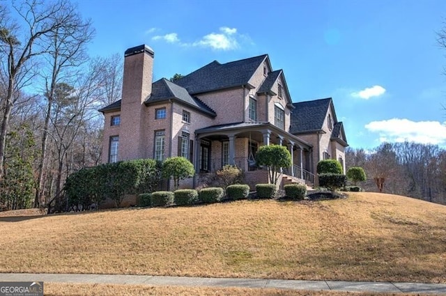 view of property exterior with brick siding, a chimney, covered porch, and a yard