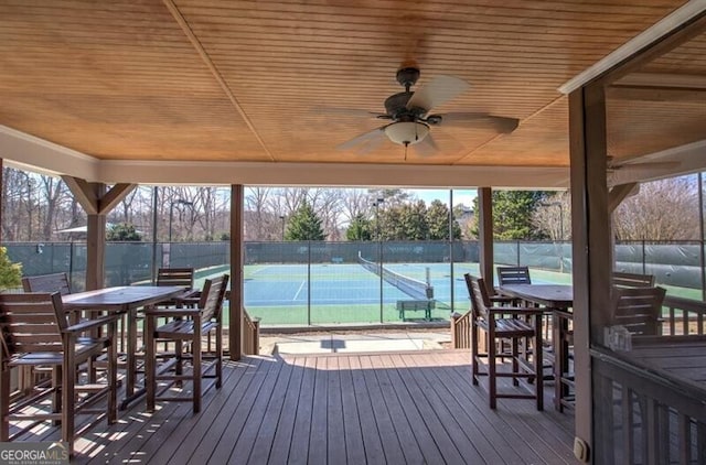 wooden deck with a ceiling fan, a tennis court, and fence