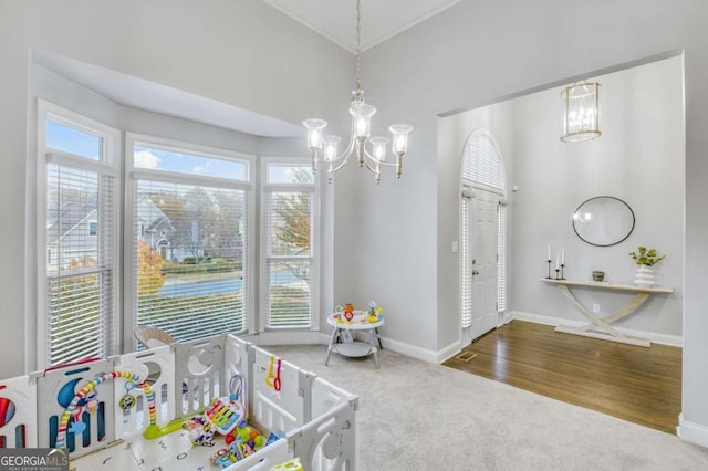 recreation room featuring carpet floors, wood finished floors, baseboards, ornamental molding, and an inviting chandelier