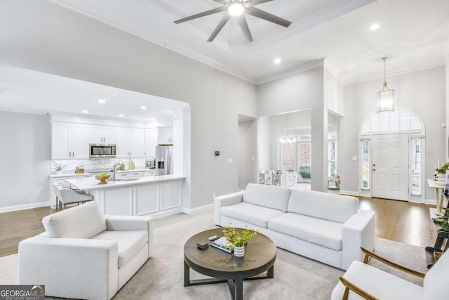 living room with baseboards, a high ceiling, a tray ceiling, crown molding, and light wood-type flooring