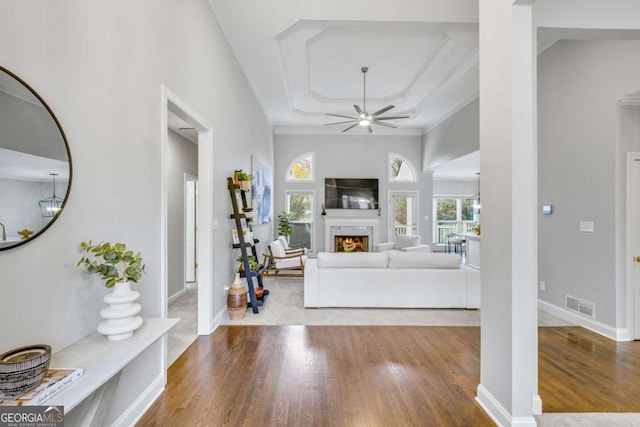 unfurnished living room featuring visible vents, a raised ceiling, ceiling fan, a premium fireplace, and wood finished floors