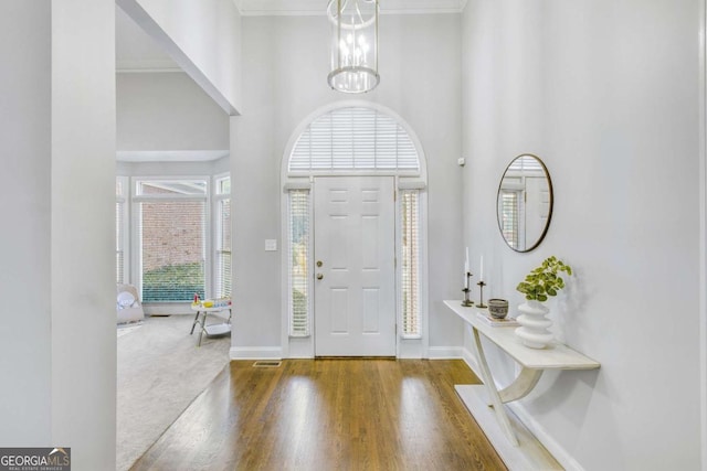 entryway featuring baseboards, a towering ceiling, wood finished floors, crown molding, and a chandelier