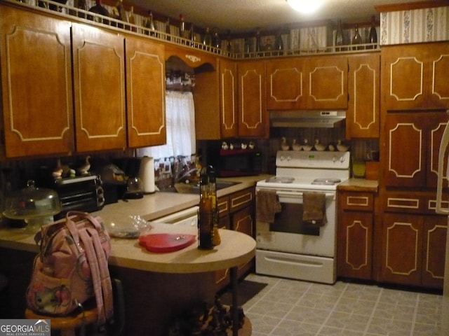 kitchen with brown cabinetry, electric range, under cabinet range hood, and light countertops