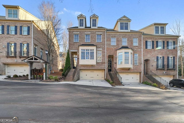 view of property with a garage, brick siding, driveway, and stairs