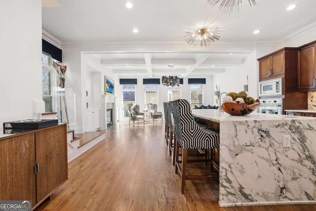 kitchen featuring appliances with stainless steel finishes, a kitchen breakfast bar, wood finished floors, a fireplace, and beam ceiling