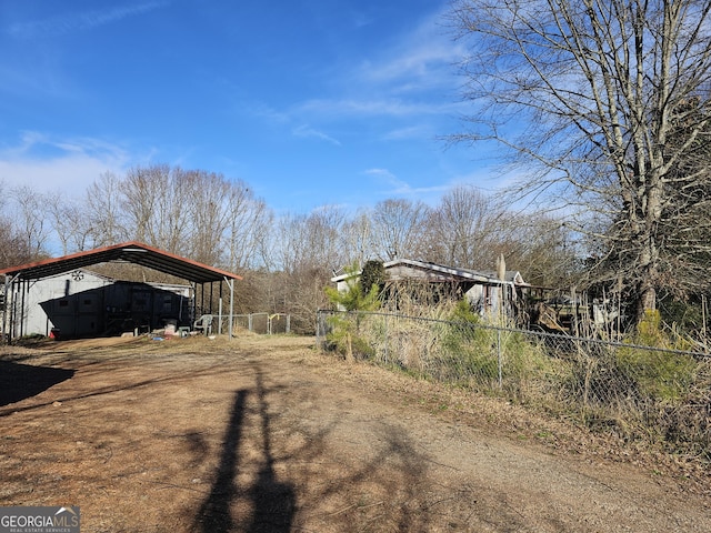 view of yard with dirt driveway, fence, and a carport