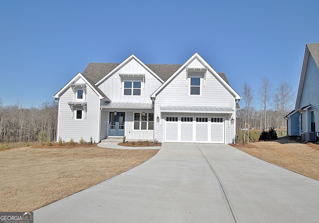 view of front facade with cooling unit, a garage, driveway, board and batten siding, and a standing seam roof