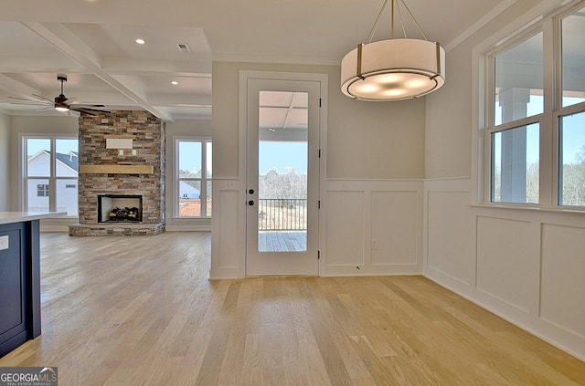 doorway to outside featuring a decorative wall, a fireplace, coffered ceiling, beam ceiling, and light wood finished floors