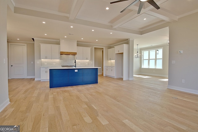 kitchen featuring open floor plan, a kitchen island with sink, custom exhaust hood, light countertops, and white cabinetry