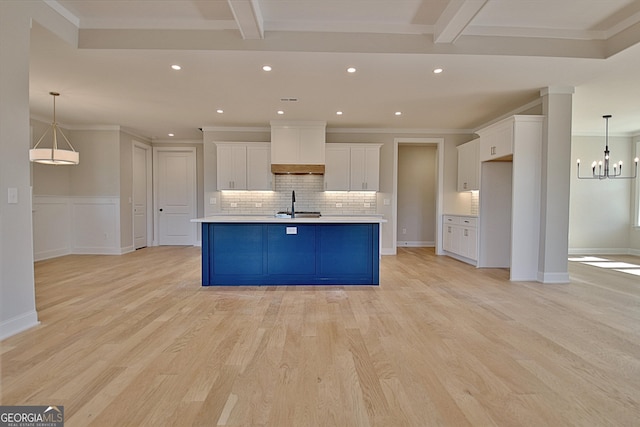 kitchen featuring a sink, white cabinetry, light countertops, hanging light fixtures, and a center island with sink