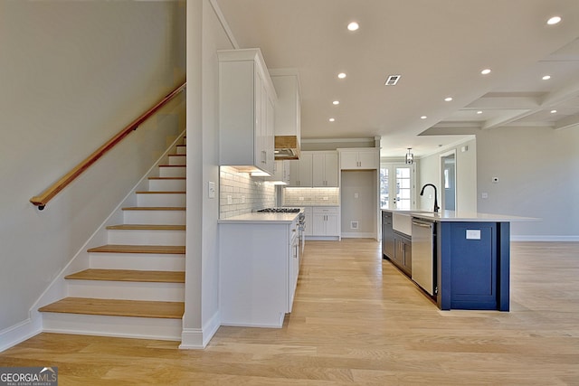 kitchen with light countertops, light wood-style floors, a kitchen island with sink, white cabinetry, and dishwasher