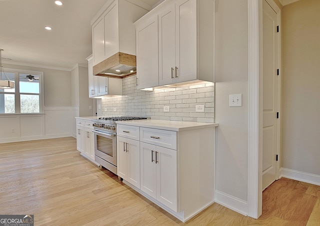 kitchen with white cabinets, light wood-type flooring, hanging light fixtures, high end stove, and premium range hood