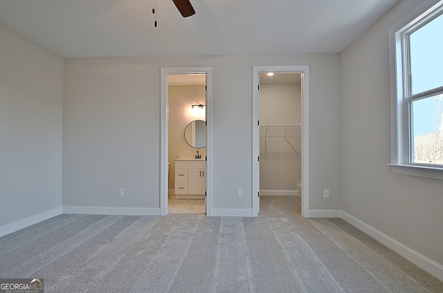 unfurnished bedroom featuring light carpet, ensuite bath, baseboards, and a walk in closet