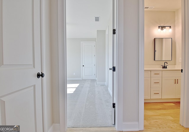 hallway with light carpet, baseboards, visible vents, and a sink