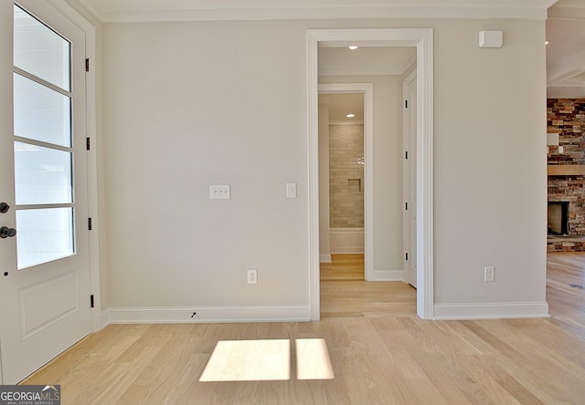 interior space with light wood-type flooring, a stone fireplace, and baseboards