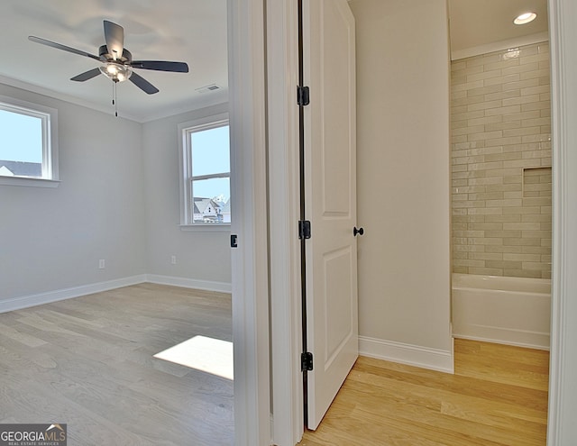 interior space featuring ceiling fan, light wood-style flooring, visible vents, baseboards, and ensuite bath