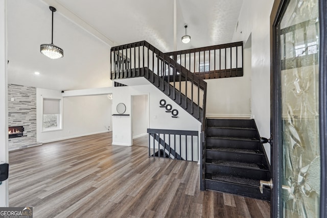 staircase with baseboards, a fireplace, high vaulted ceiling, and wood finished floors