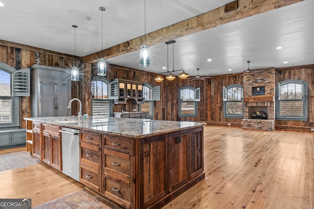 kitchen with beam ceiling, a brick fireplace, a sink, a large island with sink, and dishwasher