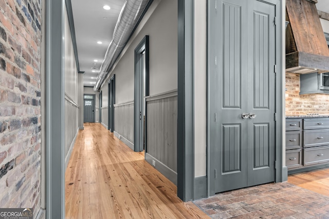 hallway featuring light wood-type flooring, brick wall, and recessed lighting