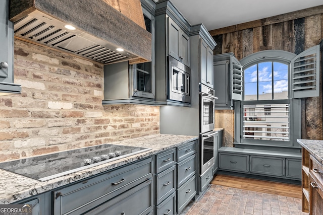 kitchen featuring brick floor, stainless steel appliances, gray cabinets, custom exhaust hood, and light stone countertops