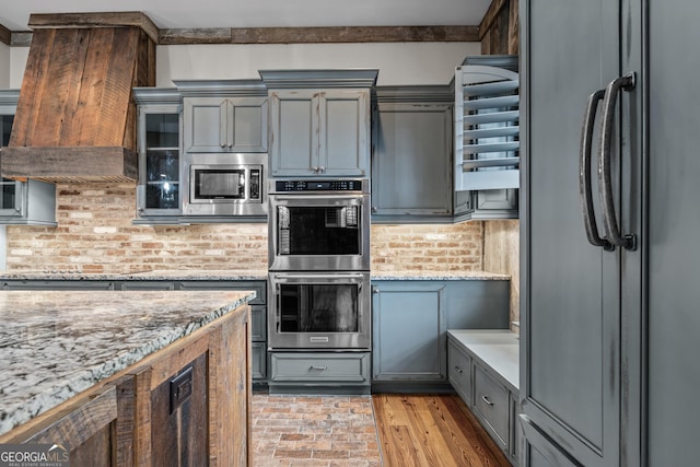 kitchen with light stone counters, gray cabinetry, glass insert cabinets, and black appliances