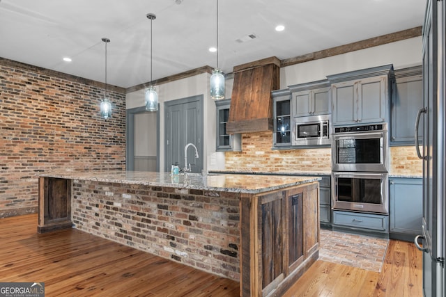 kitchen with brick wall, stainless steel appliances, light wood-type flooring, and a sink