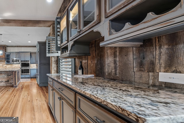 kitchen with glass insert cabinets, appliances with stainless steel finishes, light stone counters, light wood-type flooring, and backsplash